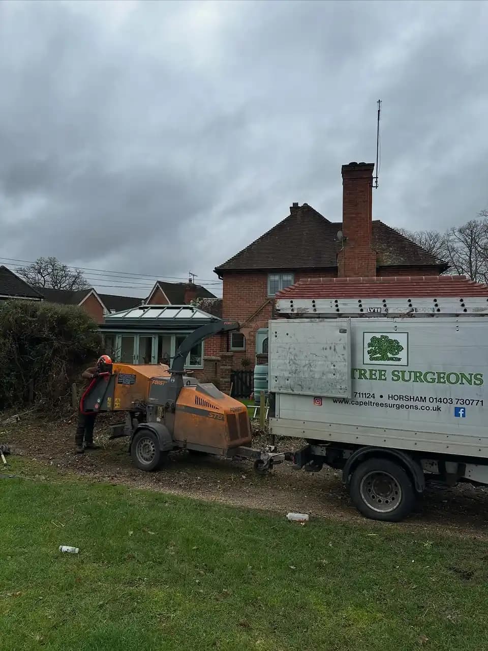 Wood chipper and truck set up beside a property during hedge and tree clearance.